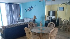 Un comedor con una mesa redonda y sillas, un sofá, un ventilador de techo y una pared con un mural de peces.