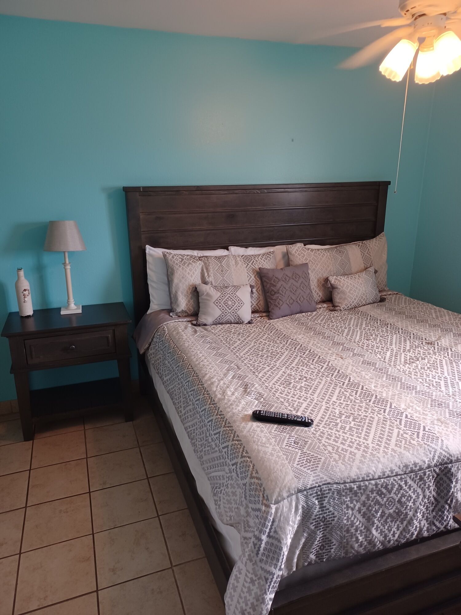 Een slaapkamer met een bed, nachtkastje, lamp en plafondventilator.