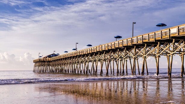 Un muelle de madera que se adentra en el agua, con sombrillas y farolas.