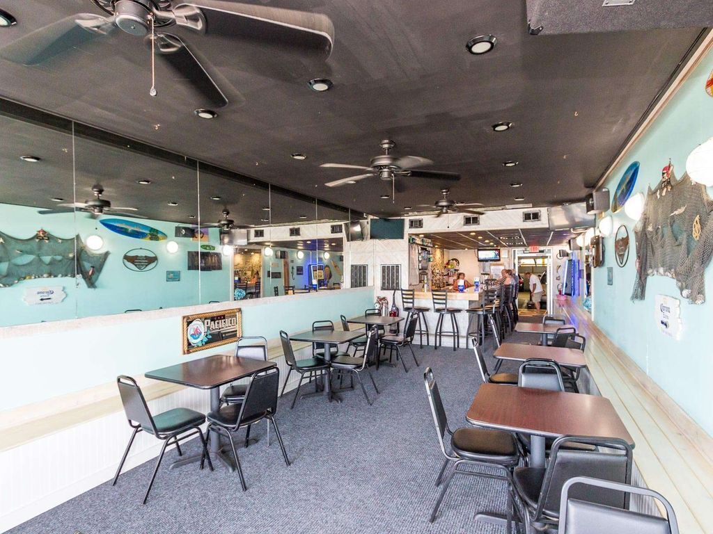 A restaurant interior with multiple tables and chairs, ceiling fans, and a mural on the wall.