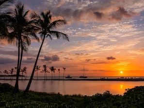 Un atardecer sobre un mar tranquilo con palmeras y un muelle.