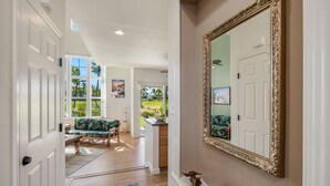 Un couloir avec un grand miroir, un bol en bois et une vue sur un jardin, visible à travers une porte vitrée.