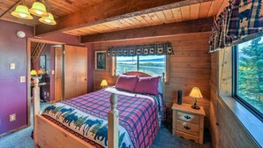 Un dormitorio de cabaña de madera con una cama, una mesita de noche, una ventana con vistas y una lámpara en el techo.