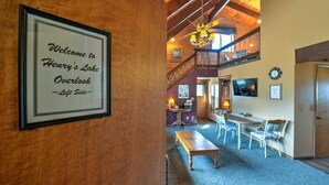 Un interior de madera con un letrero de bienvenida enmarcado, una zona de comedor y una escalera que conduce a un nivel superior.