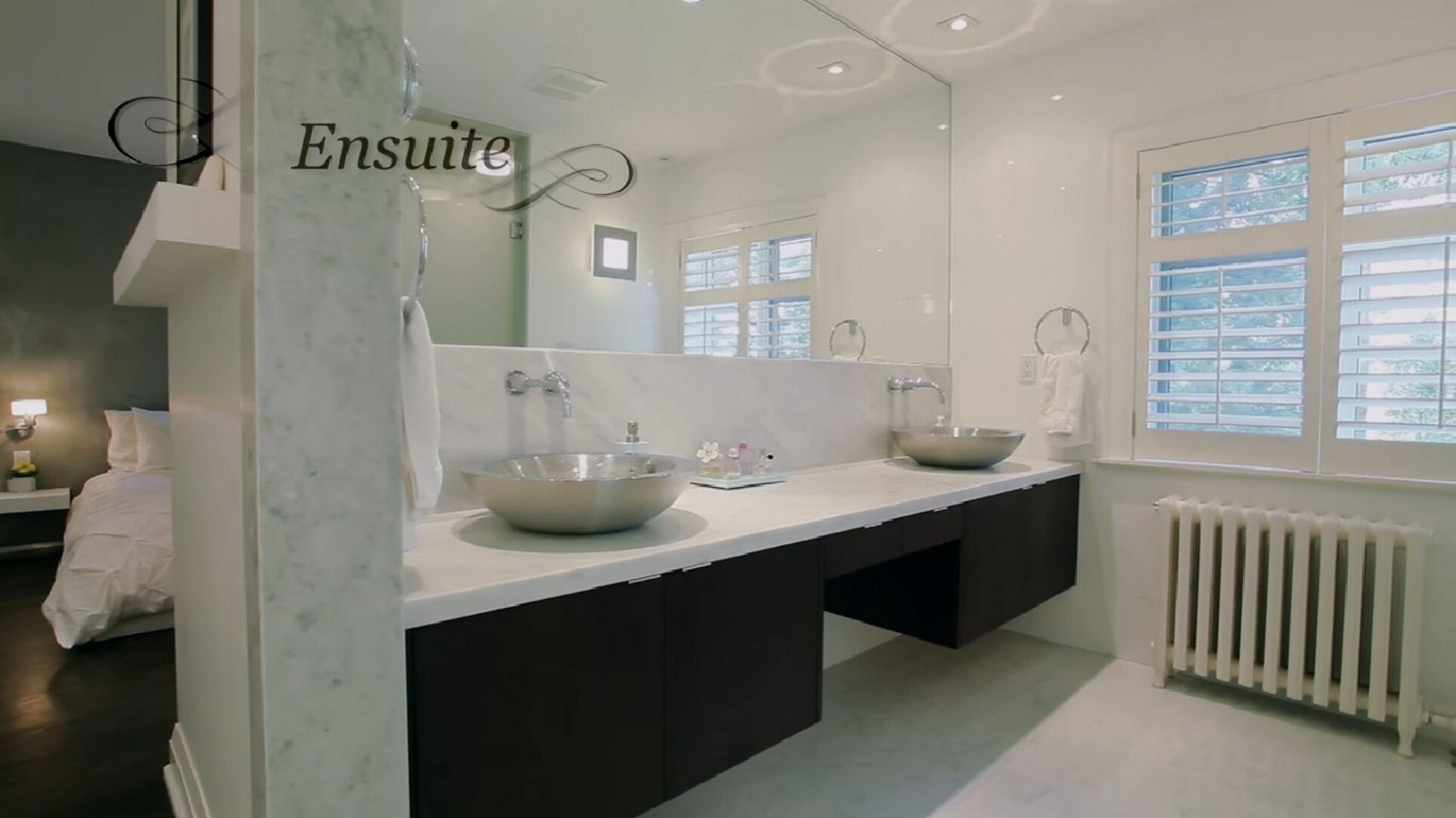 A modern bathroom with a large mirror, two sinks, and a window with blinds.