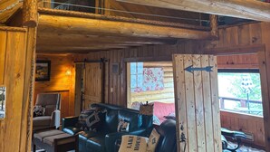 Un intérieur en bois avec un plafond haut, un lustre, un canapé et une grande fenêtre.