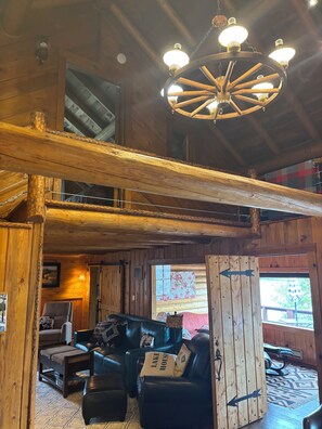 Un intérieur en bois avec un plafond haut, un lustre, un canapé et une grande fenêtre.