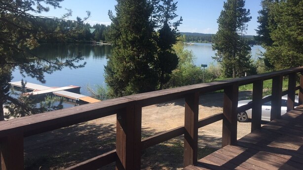 Une terrasse en bois donnant sur un lac, bordée de grands arbres et dotée d’un quai.