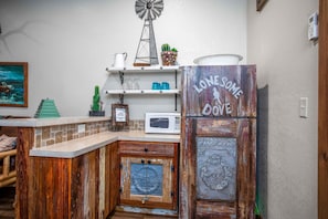 Une cuisine rustique avec un moulin à vent, un réfrigérateur orné d’une étiquette « Lonesome Dove », et un four à micro-ondes.