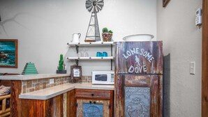 A rustic kitchen with a windmill, a refrigerator with 'LONEMOME DOVE' written on it, and a microwave. - Lonesome Dove Guesthouse (Bandera)