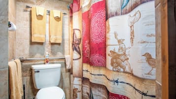 A bathroom with a toilet, a towel rack with towels, and a shower curtain with a patterned design.