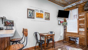 A rustic interior with wooden furniture, a mounted TV, and wall decorations including framed pictures and a sign. - Lonesome Dove Guesthouse (Bandera)