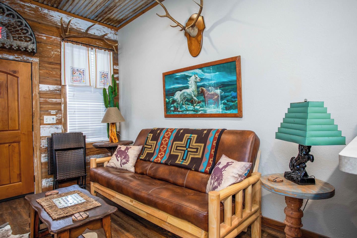 Ein rustikales Wohnzimmer mit einer Ledersofa, Holmöbeln, einer Kakteenpflanze und einem an der Wand befestigten Hirschkopf.