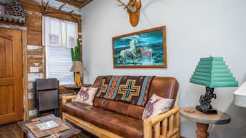 Ein rustikales Wohnzimmer mit einer Ledersofa, Holmöbeln, einer Kakteenpflanze und einem an der Wand befestigten Hirschkopf.