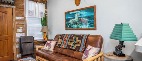 A rustic living room with a leather sofa, wooden furniture, a cactus plant, and a wall-mounted deer head.