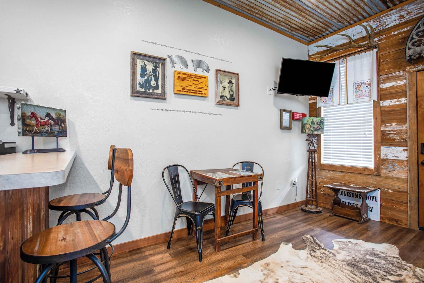 A room with a wooden table, two chairs, a mounted television, and wall-mounted artwork.