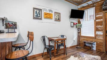 A room with a wooden table, two chairs, a mounted television, and wall-mounted artwork.