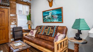 A rustic living room with a leather sofa, a cactus, a mounted deer head, and a painting of a horse. - Lonesome Dove Guesthouse (Bandera)