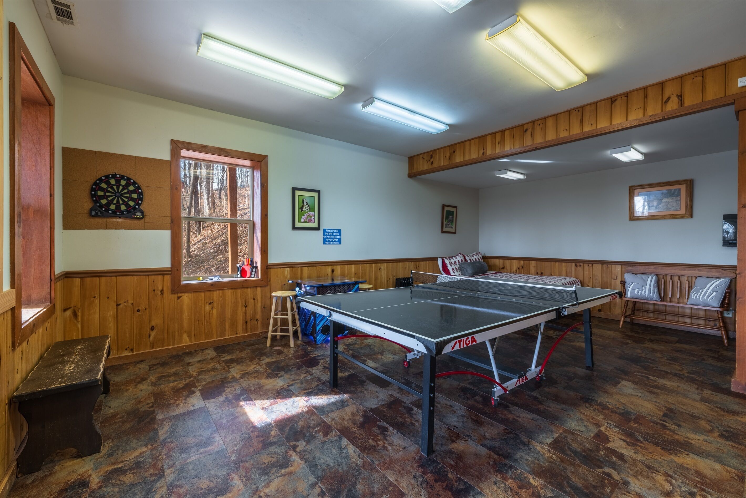 Une pièce avec une table de ping-pong, un jeu de fléchettes, des murs en bois, une fenêtre et un banc.