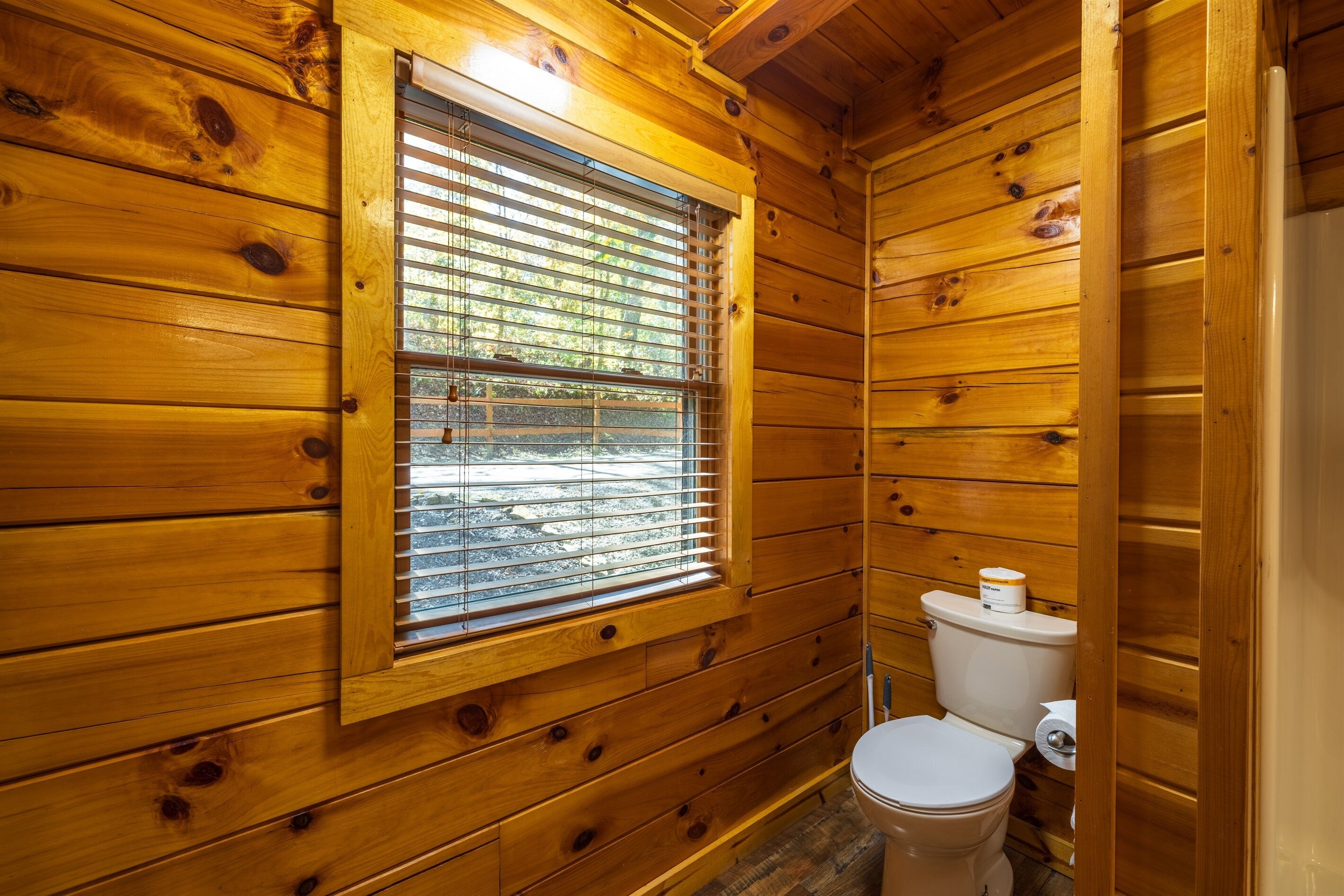 Een houten badkamer met raam, toilet en houten wanden.
