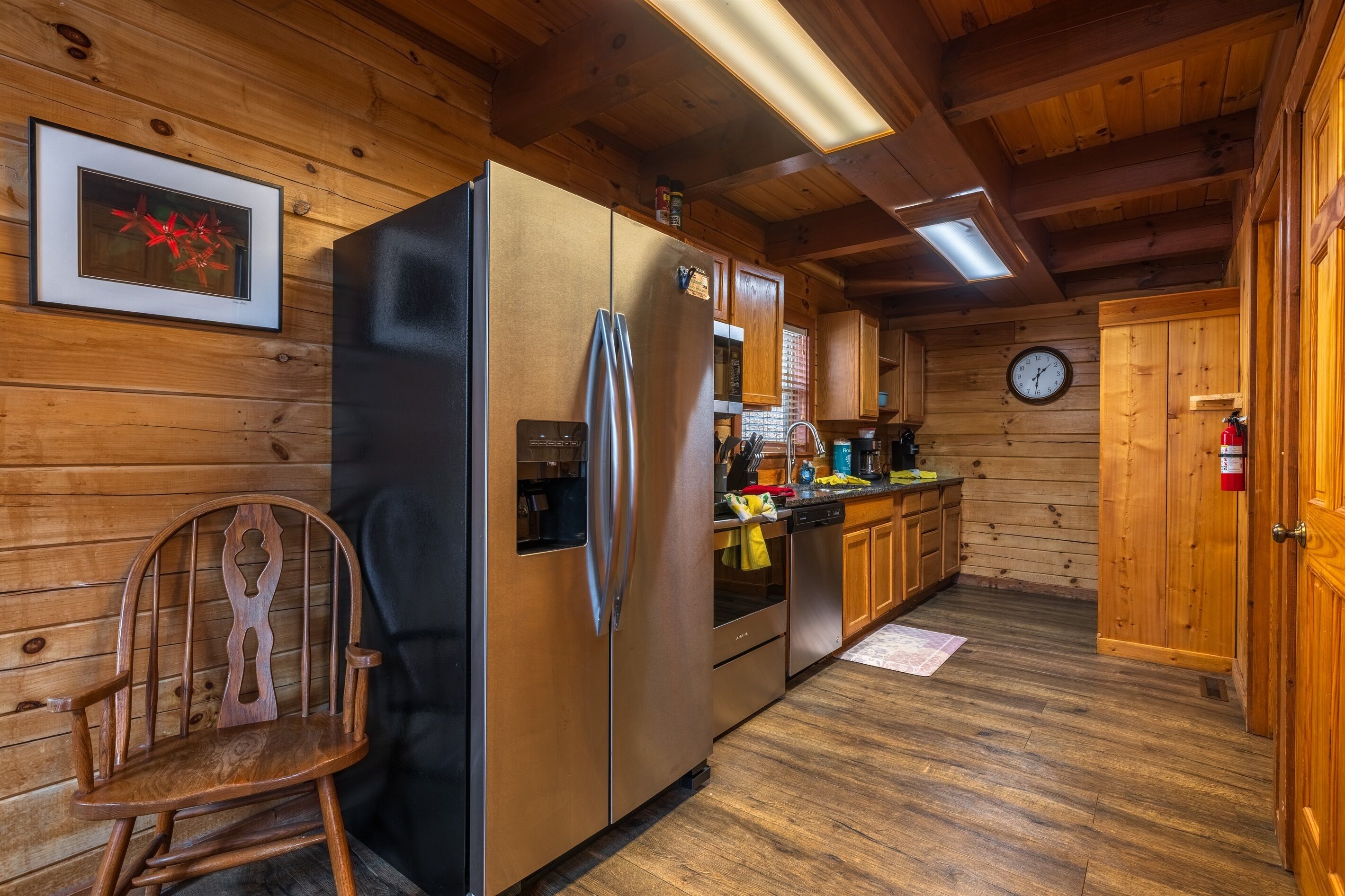 Ein Holzblockhaus-Interieur mit einem großen Edelstahl-Kühlschrank, Holzausstattung, einem Holzschaukelstuhl und einer Uhr an der Wand.