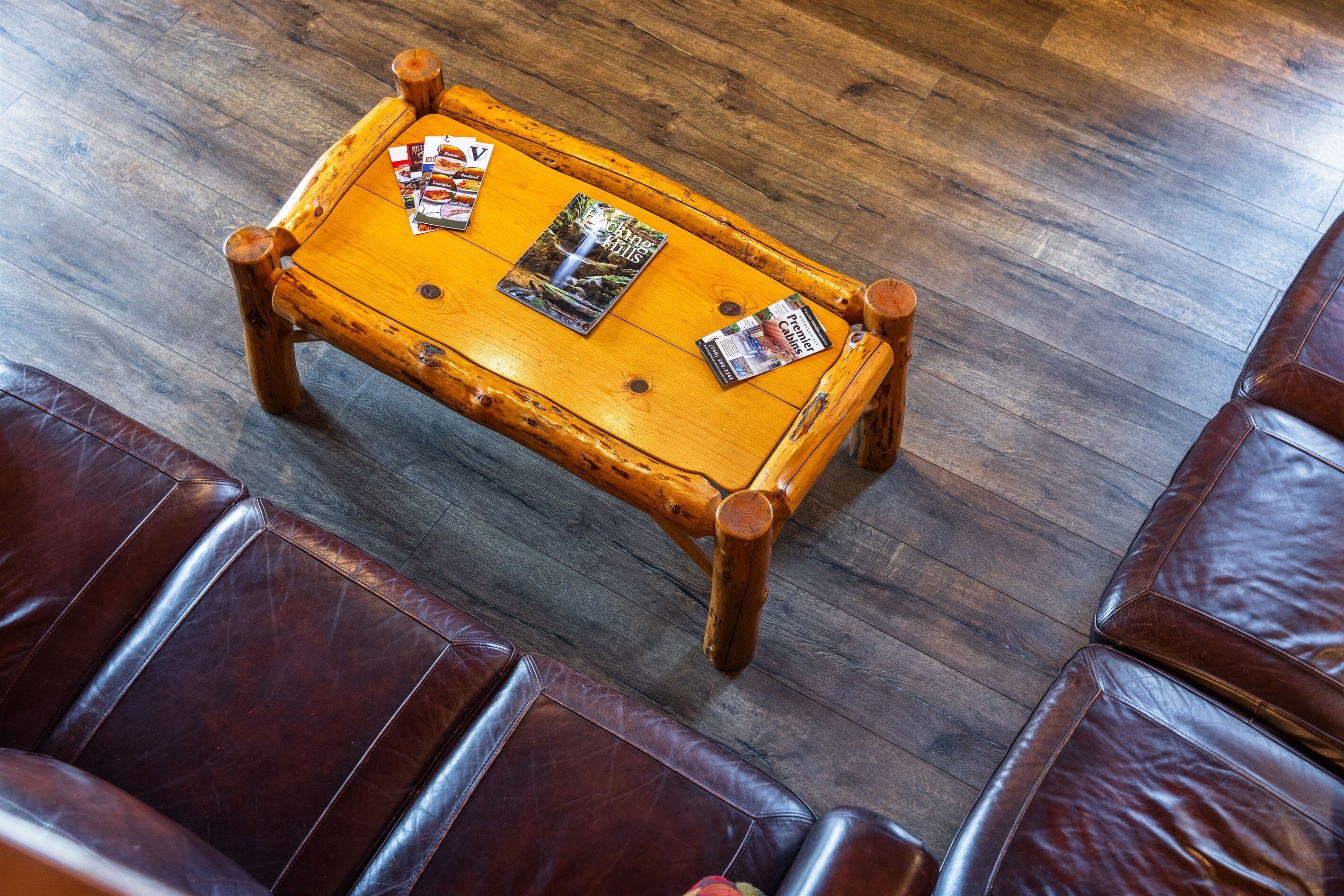 Una mesa de centro de madera con revistas y un vaso de bebida sobre un suelo de madera.