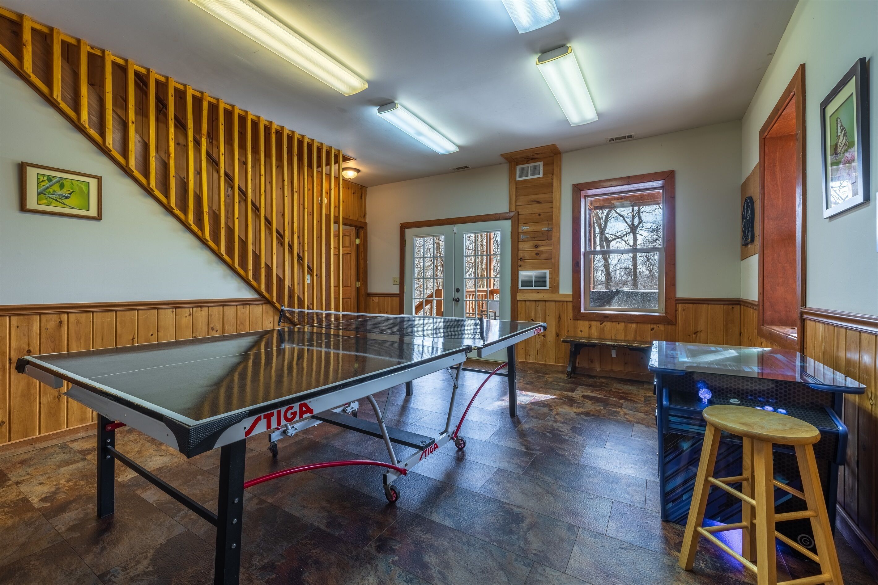 Una mesa de ping pong, una escalera de madera y una zona de bar en una habitación con paredes y ventanas de madera.