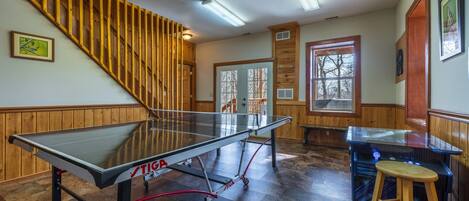 Una mesa de ping pong, una escalera de madera y una zona de bar en una habitación con paredes y ventanas de madera.