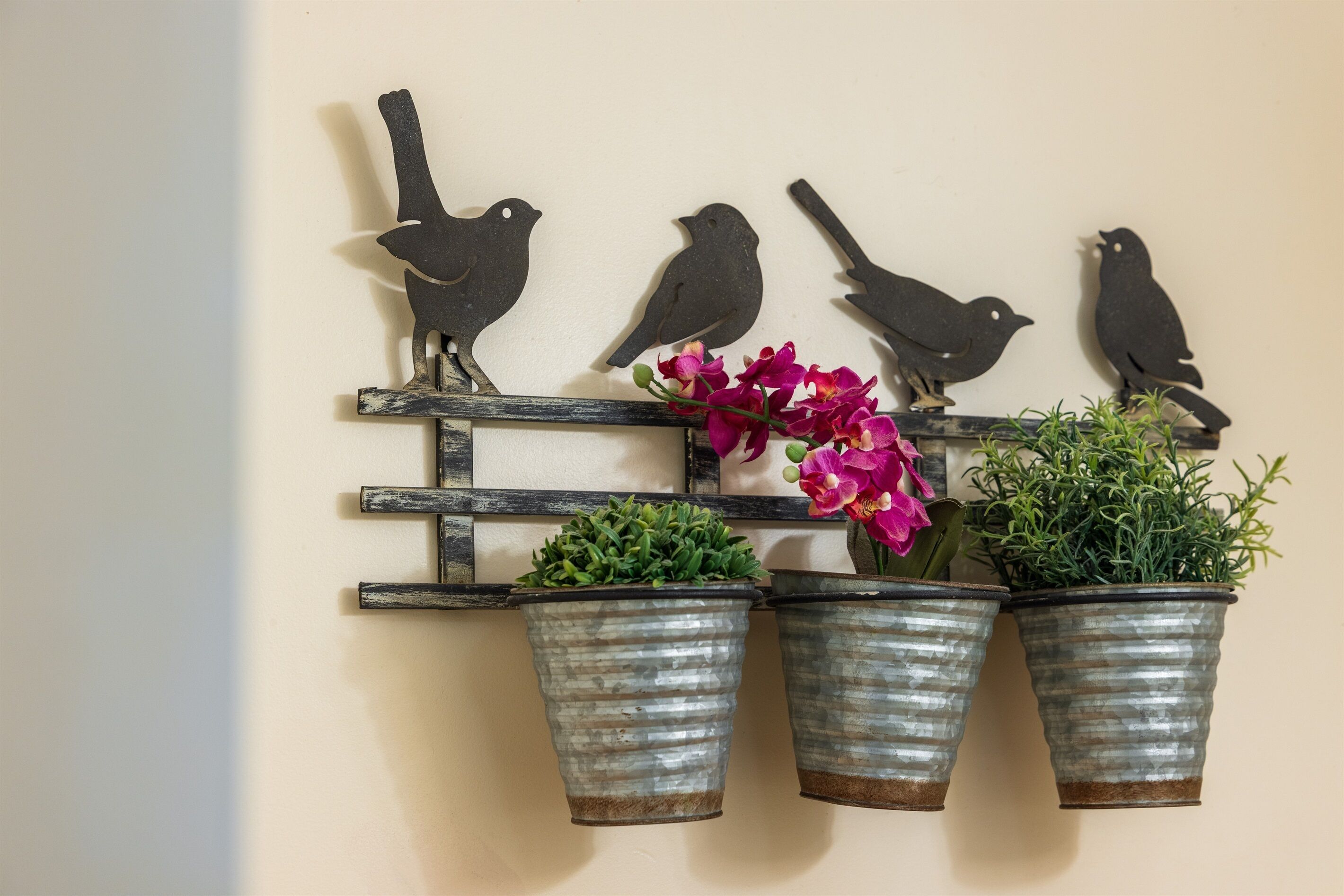 Een wanddecoratie van een vogelbeeldje met daaronder drie plantenpotten.