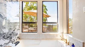 A bathroom with a marble sink, a bathtub, and two windows overlooking a patio with outdoor furniture and an umbrella. - Resort-like Villa, 50' Infinity Edge Pool, Garden, Peaceful, Luxurious (Sonoma)