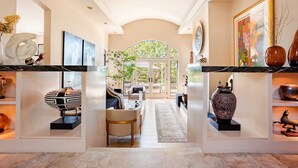 A spacious living area with a central seating arrangement, a fireplace, and a view through an arched doorway to an outdoor space. - Resort-like Villa, 50' Infinity Edge Pool, Garden, Peaceful, Luxurious (Sonoma)