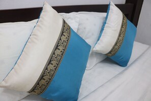 Una cama con ropa blanca y dos almohadas, una blanca y otra azul, con un borde decorativo.