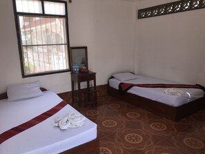 Habitación de hotel con dos camas, una mesita con un espejo y una ventana con barrotes.