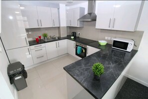 A modern kitchen with white cabinets, a black countertop, a microwave, and a small potted plant. - BlueOne Serviced Apts - Kelham Island (Sheffield)
