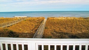A beach view with a wooden boardwalk leading to the ocean, surrounded by grassy dunes.
