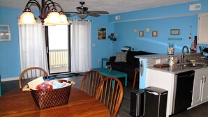 A compact kitchen with a dining area, a ceiling fan, and a window with curtains.