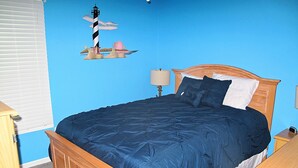 A bedroom with a wooden bed, a nightstand, a lamp, and a wall decoration of a lighthouse.