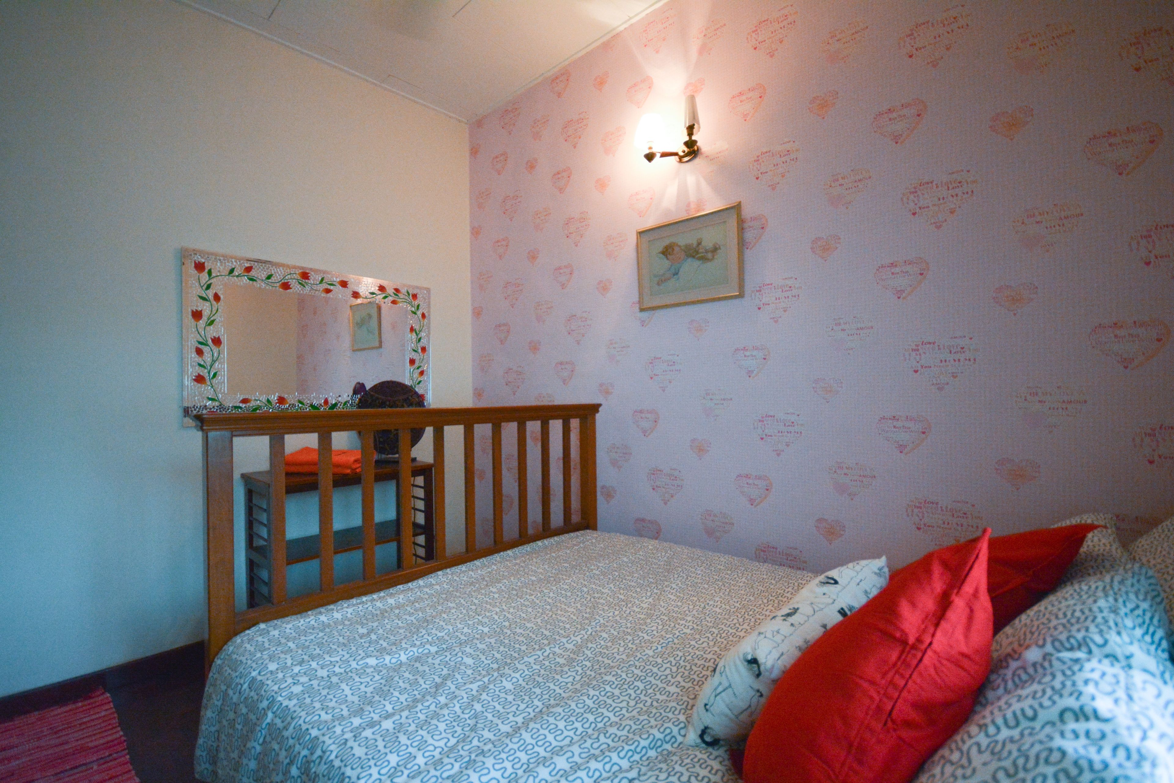 A bedroom with a wooden crib, a bed with patterned bedding, a wall with heart designs, and a framed picture.