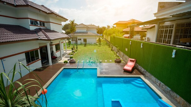 Uma piscina com escorregador, cercada por um muro verde e um gramado bem cuidado.