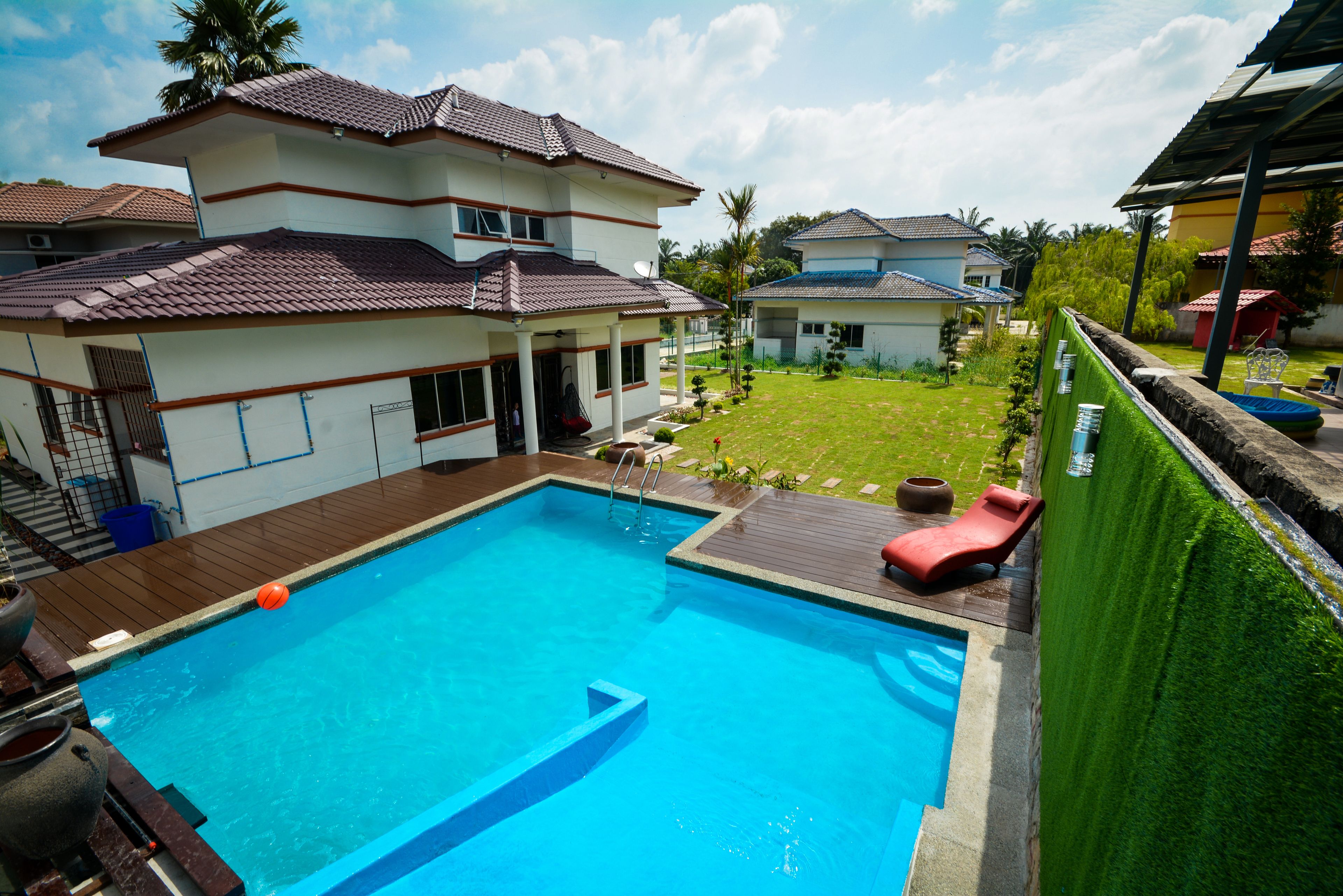 A rectangular swimming pool with a wooden deck, surrounded by a green hedge.
