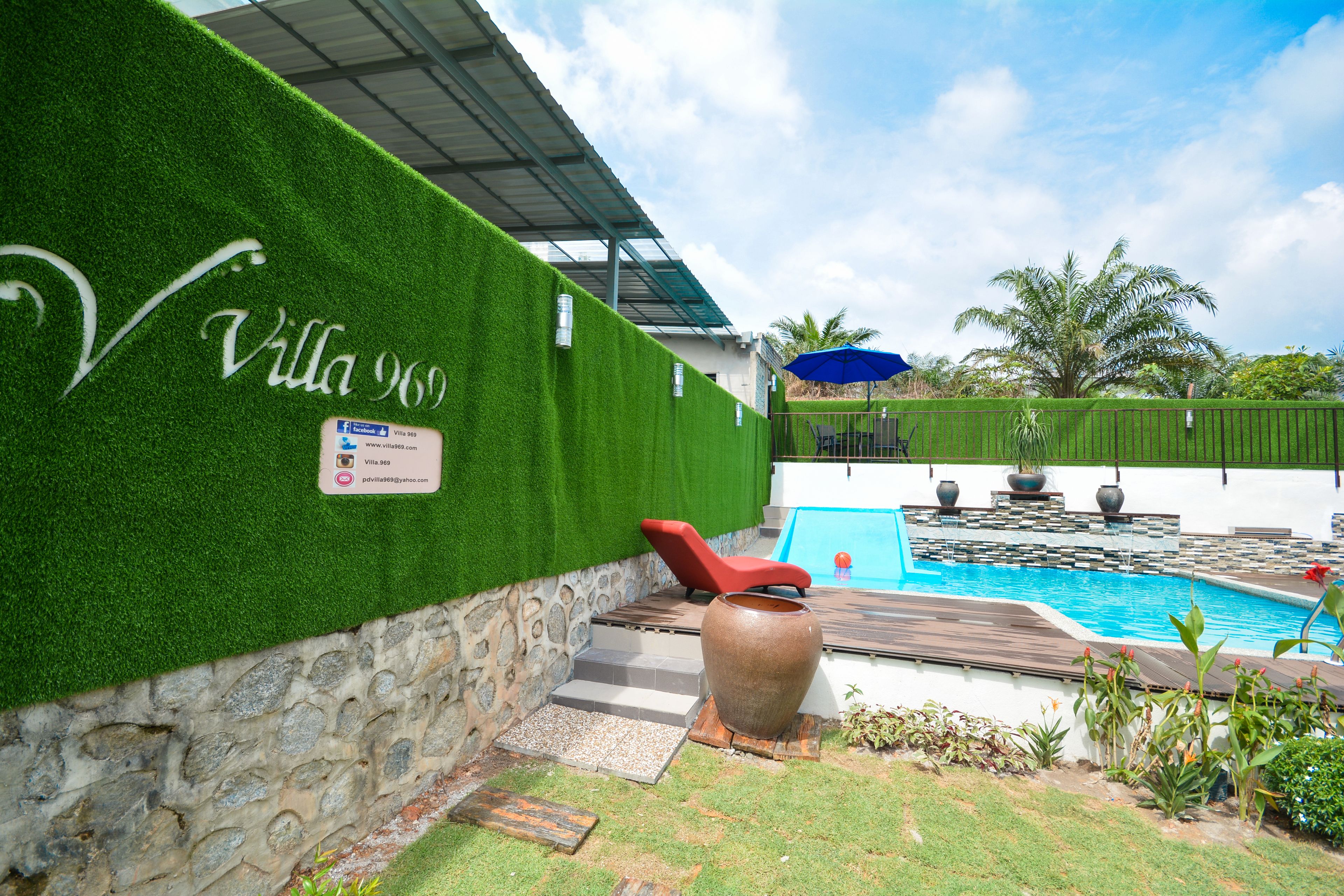 A pool area with a green wall, a red lounge chair, and a large planter.
