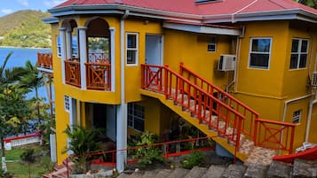 Ein gelbes Gebäude mit rotem Dach, eine Treppe mit roten Geländern und Blick auf das Meer.