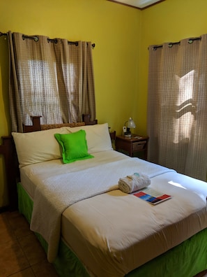 A neatly made bed with a green pillow, a rolled towel, and a brochure on the bed. - Sunset Lane (Laborie)