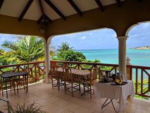 A covered outdoor area with a table and chairs, a small table with a white tablecloth, and a view of the ocean.