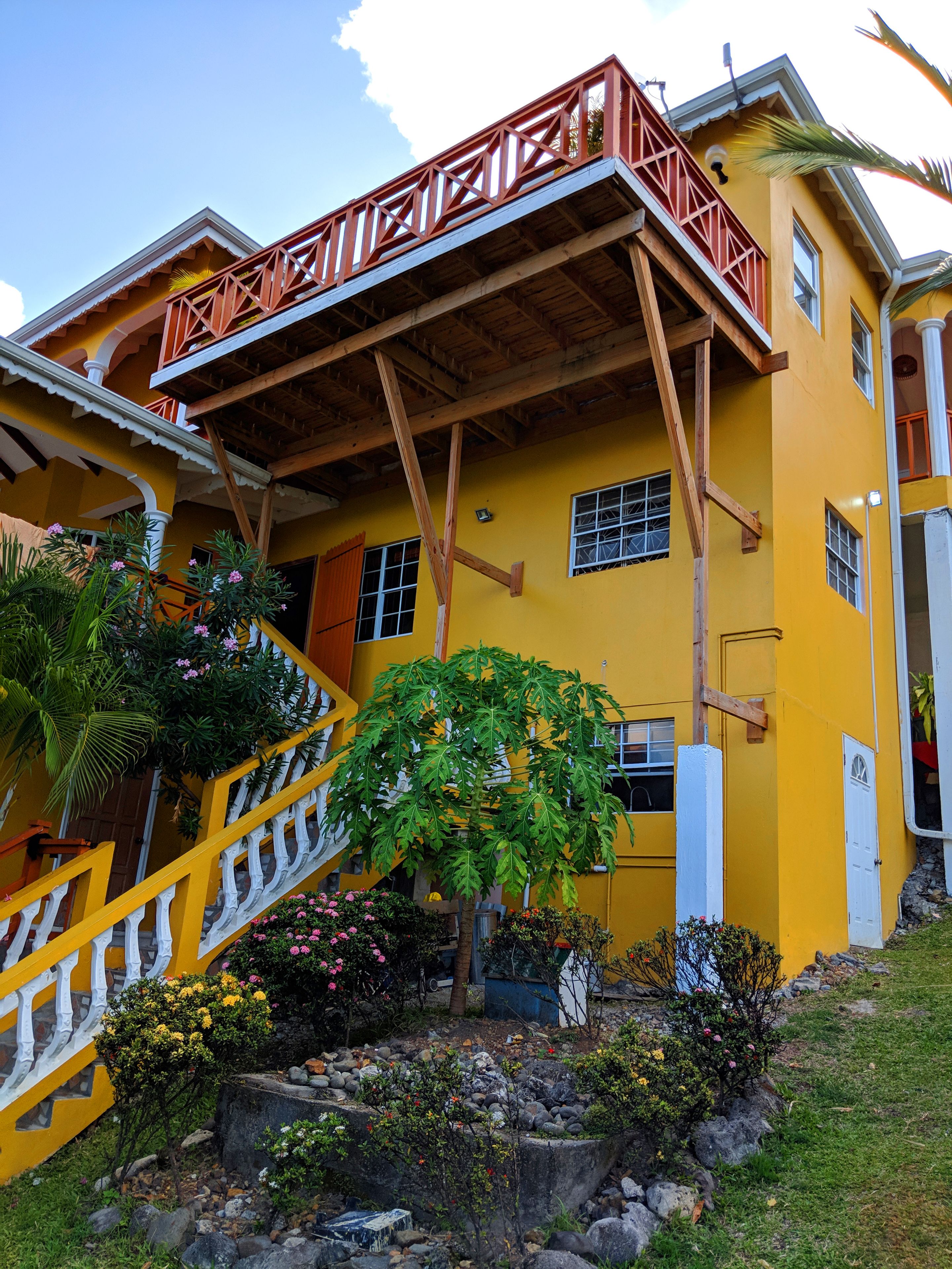 A yellow building with a wooden balcony and a staircase leading to the entrance.