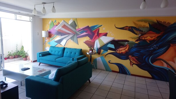 A living room with a teal sofa, a coffee table, and a vibrant abstract mural on the wall. - Beautiful luxury apartment near (Zone 16)