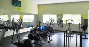 A gym with exercise equipment, large windows, and a television on the wall.