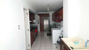 A narrow kitchen with wooden cabinets, a stainless steel refrigerator, and a white washing machine. - Beautiful luxury apartment near (Zone 16)