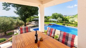 Un tavolo in legno con una bottiglia e un bicchiere, vista su una piscina e vegetazione lussureggiante.