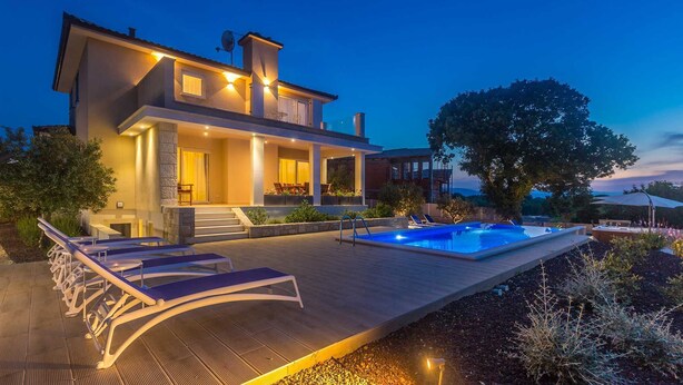 Una casa moderna a due piani con piscina, area salotto esterna e un grande albero sullo sfondo.